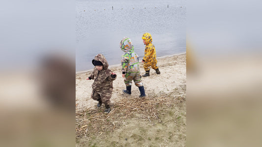 Drie kinderen in kleurrijke buitenspeelpakken bij het water